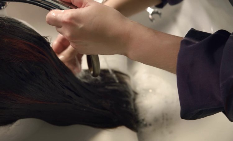 La imagen muestra a una mujer lavándose el pelo en una peluquería, ilustrando así el programa de salud mental de L’Oréal para profesionales del cabello.