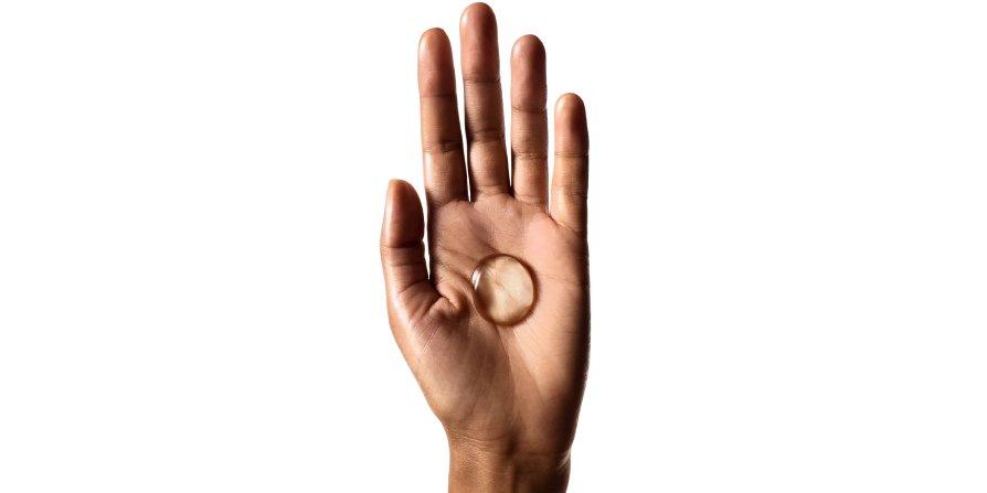 La imagen muestra una mano sosteniendo una gota de champú, ilustrando que usar la cantidad y el método de aplicación adecuados ayuda a reducir la grasa en el cabello.