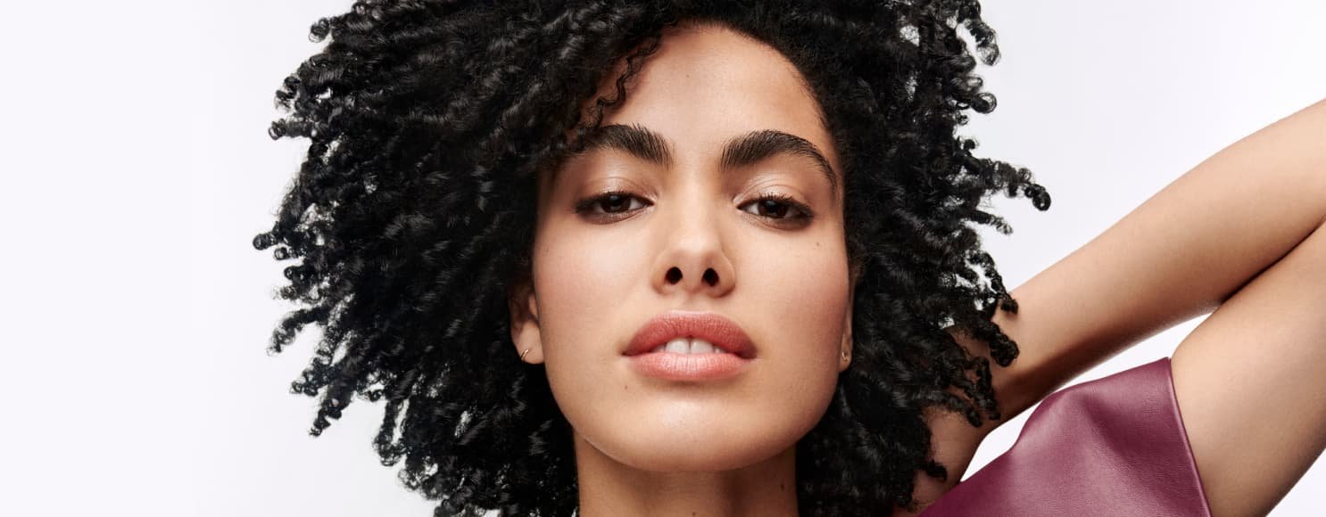 Mujer posando y mostrando su cabello oscuro y rizado bien definido, con un aspecto saludable, volumen y una textura natural realzada.