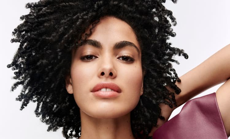 Mujer posando y mostrando su cabello oscuro y rizado bien definido, con un aspecto saludable, volumen y una textura natural realzada.