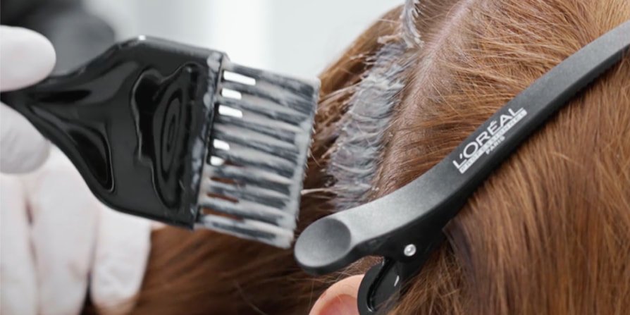 La escena se centra en una mujer en la peluquería a la que una profesional le está tiñendo el pelo, mostrando cómo conseguir el moderno color castaño espresso.