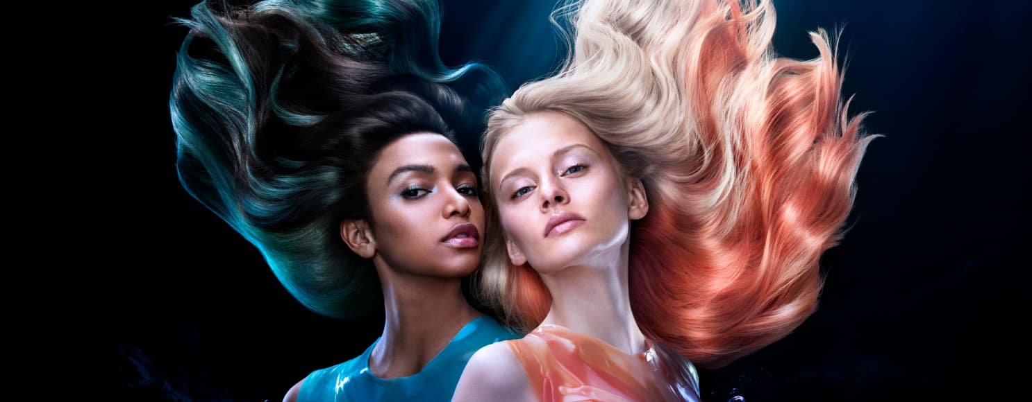 Dos mujeres posando, una con cabello rubio y mechones naranjas, la otra con cabello oscuro y reflejos azules intensos.