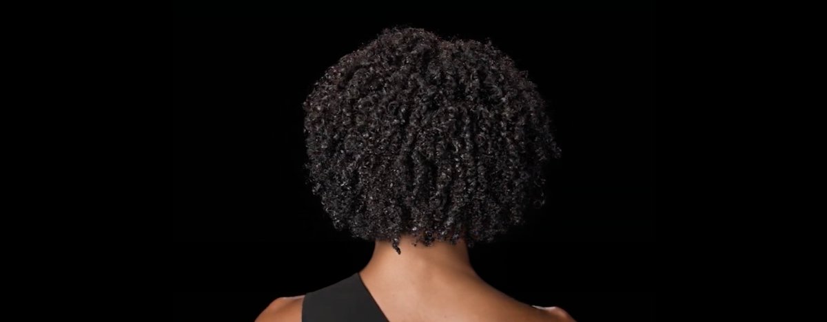 Mujer de espaldas con cabello rizado brillante y sano, que muestra consejos y técnicas para desenredar los rizos sin dañarlos.