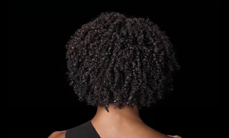 Mujer de espaldas con cabello rizado brillante y sano, que muestra consejos y técnicas para desenredar los rizos sin dañarlos.