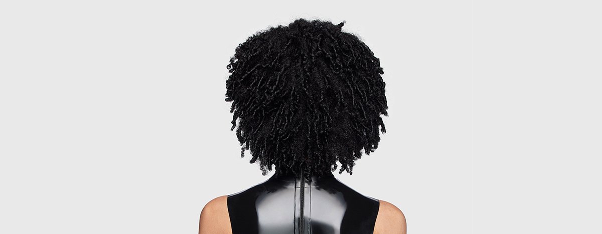 Mujer de espaldas con rizos definidos, brillantes y sanos, que muestra consejos y técnicas de cuidado para mantener un cabello rizado y nutrido.