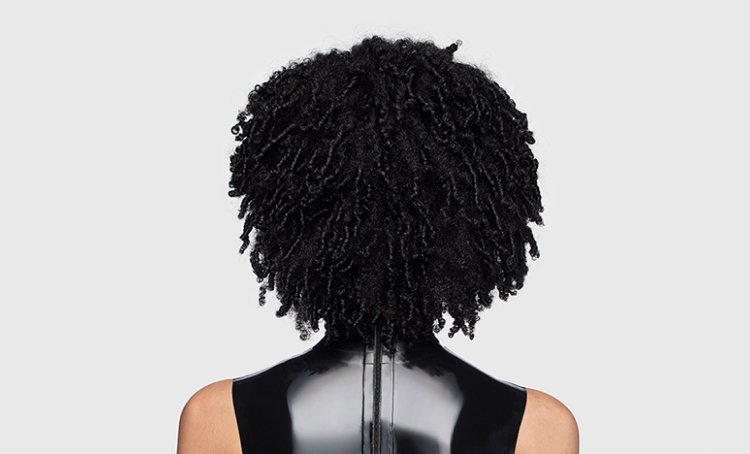 Mujer de espaldas con rizos definidos, brillantes y sanos, que muestra consejos y técnicas de cuidado para mantener un cabello rizado y nutrido.